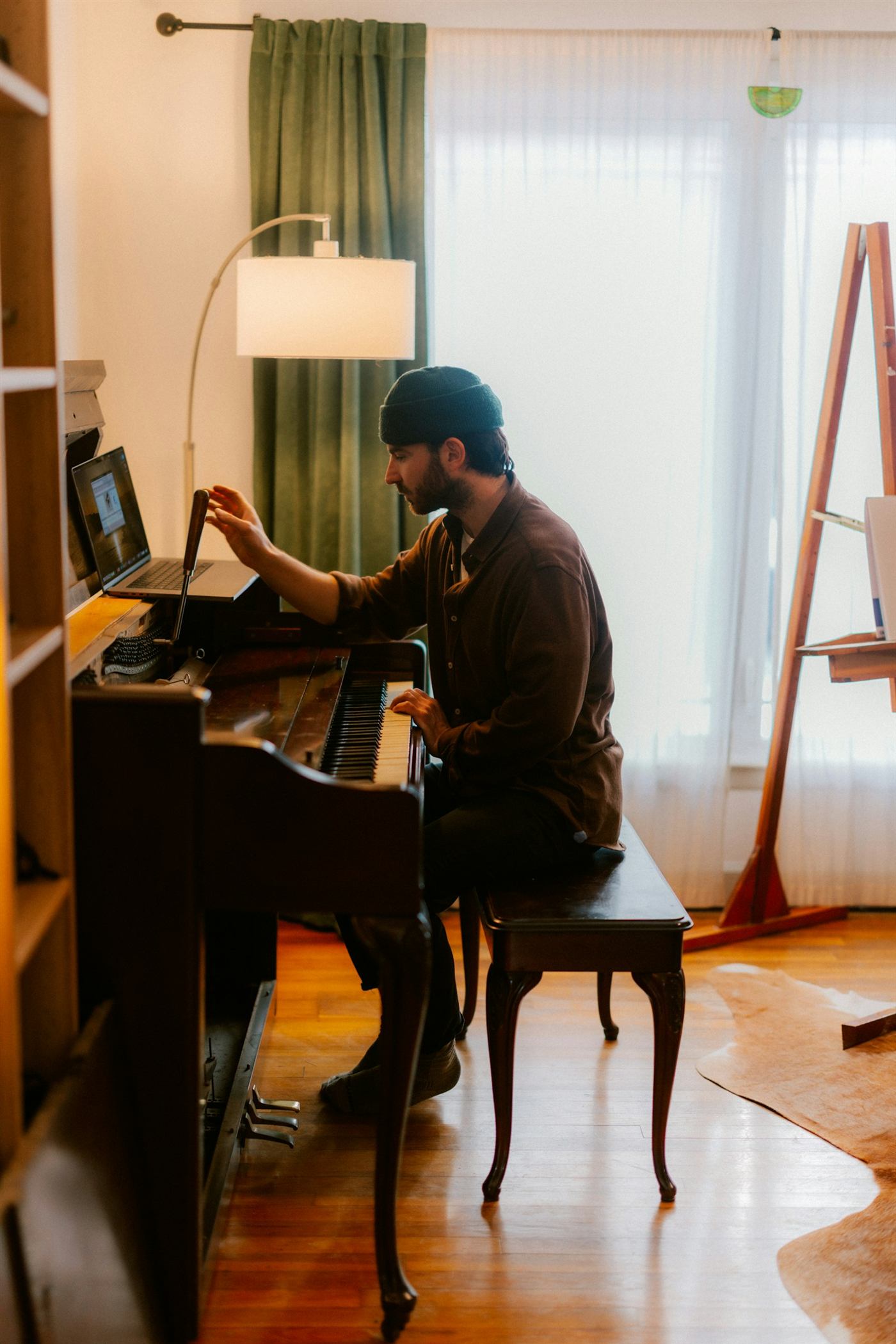 A musician learning at the piano with a laptop beside the instrument